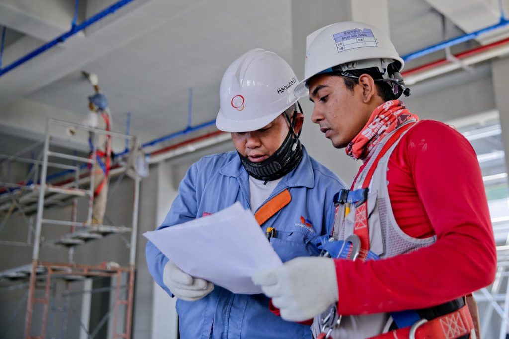 pexels-photo-1216589 Two engineers in safety helmets reviewing construction plans at a worksite.
